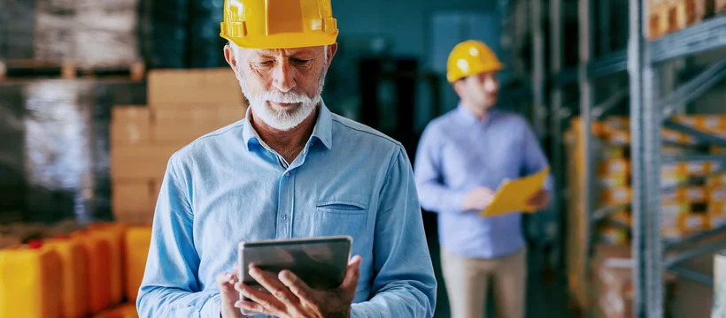 Old man with hard hat looking at tablet. Digital transformation in the logistics industry.